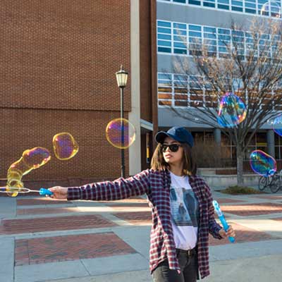 a student blowing bubbles in front of the cabell library on the v.c.u. monroe park campus