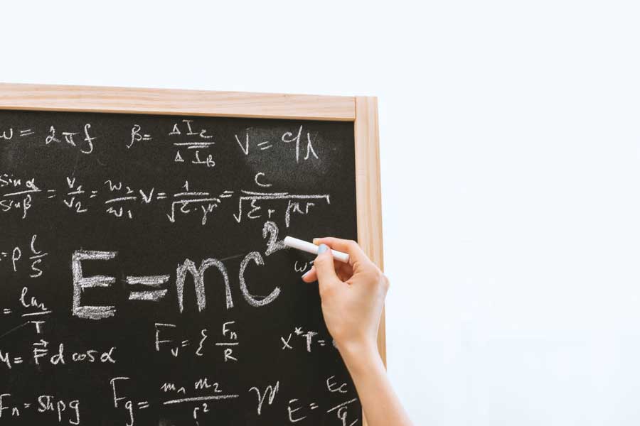 person writing physics equations on a blackboard